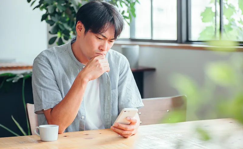 男性がスマホ操作しながら悩んでいる画像
